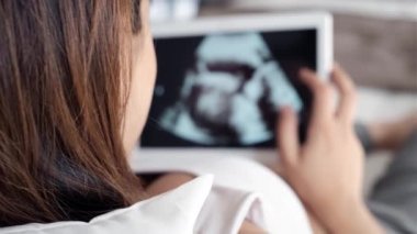 Yatakta yatarken dijital tablette bebeğinin ultrason görünümlü güzel genç hamile kadının Video.