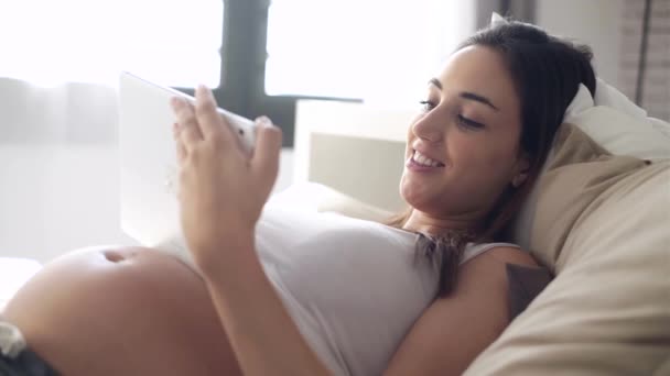 美丽的年轻孕妇使用她的数字平板电脑 而躺在家里的床上的视频 — 图库视频影像