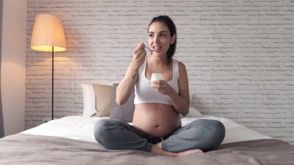 Видео Красивой Молодой Беременной Женщины Которая Ест Йогурт Сидя Дома — стоковое видео
