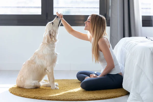 Flot ung kvinde fodrer sin hund, mens hun har det sjovt hjemme . - Stock-foto