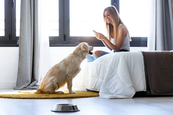 Jolie jeune femme utilisant son téléphone portable tout en restant avec son chien à la maison . — Photo