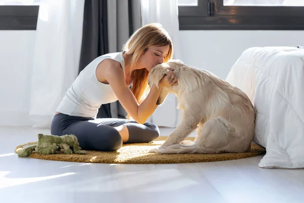 Mujer bastante joven besando a su perro mientras está sentada en el suelo en casa . — Foto de Stock