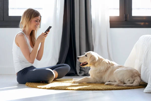 Mujer bastante joven tomando fotografías a su perro mientras se queda en el suelo en casa . — Foto de Stock