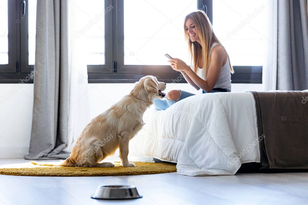 Pretty young woman using her mobile phone while staying with her dog at home.