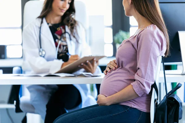 Jolie jeune femme gynécologue examinant les documents de sa patiente enceinte à la clinique . — Photo