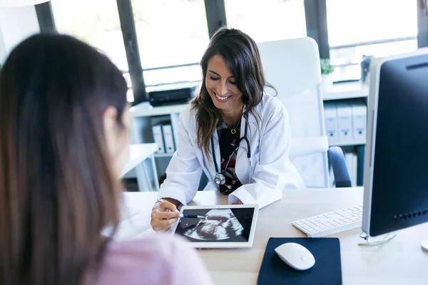 Mooie jonge vrouw gynaecoloog met behulp van digitale tablet voor het tonen van de echografie naar haar zwangere patiënt in de kliniek. — Stockfoto