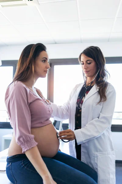 Mladá žena gynekoložka kontroluje tlukot dítěte jejího těhotného pacienta na klinice.. — Stock fotografie