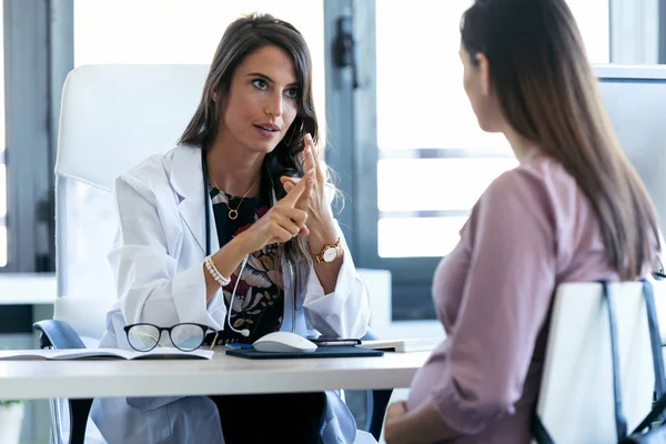 Grave giovane ginecologo che dà linee guida alla sua paziente incinta in clinica . — Foto Stock