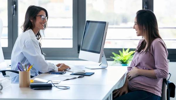Pretty young woman gynecologist reviewing the medical history of her pregnant patient with computer in the clinic. — Stock Photo, Image