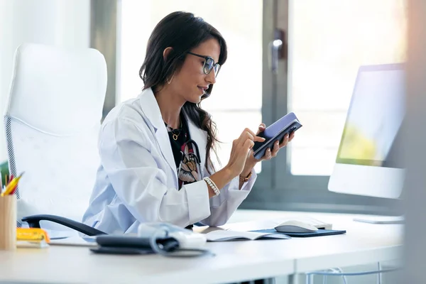 Mooie jonge vrouw gynaecoloog met behulp van haar mobiele telefoon voor aanvang van de consultatie in de kliniek. — Stockfoto