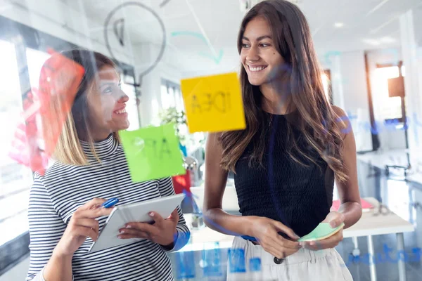 Två företag unga kvinnor som arbetar tillsammans på vägg glas med post it klistermärken i modern Startup Office. — Stockfoto