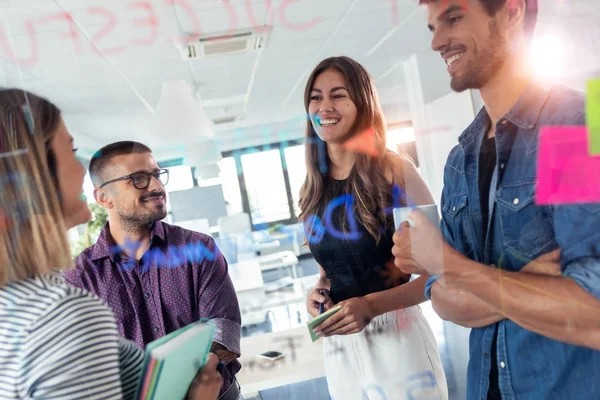 Exitoso equipo de negocios discutiendo juntos frente a la placa de vidrio de la oficina en el espacio de coworking . — Foto de Stock