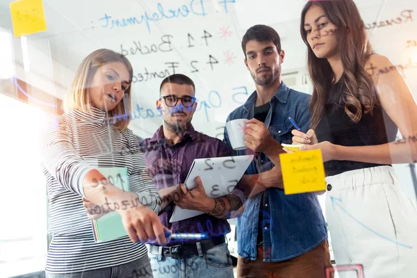 Successful business team writing on stickers at office glass board while discussing together in the coworking space. — Stock Photo, Image