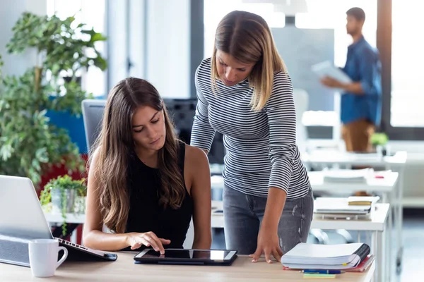 Deux jeunes femmes d'affaires travaillant ensemble avec une tablette numérique dans le bureau de démarrage moderne . — Photo