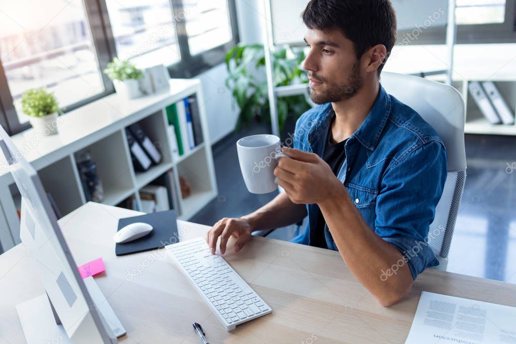 Software developer drinking coffee while working with computer in the modern startup office.