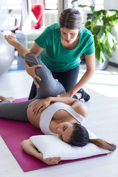 Fisioterapeuta ayudando a una hermosa mujer embarazada para hacer ejercicios de pilates preparándose para el parto . — Foto de Stock