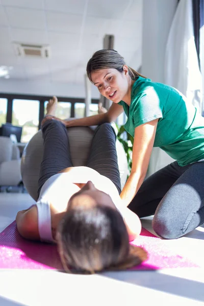 Physiotherapist helping to beautiful pregnant woman for doing pilates exercises with ball preparing for childbirth. — Stock Photo, Image