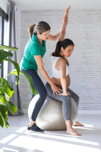 Fisioterapeuta ayudando a una hermosa mujer embarazada para hacer ejercicios de pilates con pelota preparándose para el parto . — Foto de Stock