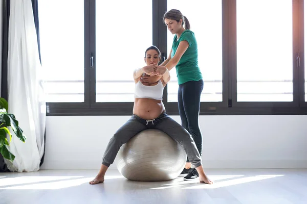 Fisioterapeuta ayudando a una hermosa mujer embarazada para hacer ejercicios de pilates con pelota preparándose para el parto . — Foto de Stock