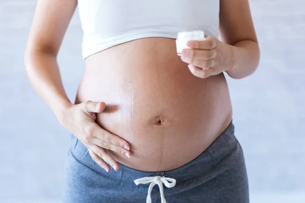 Mulher grávida aplicando creme loção na barriga grávida para evitar estrias . — Fotografia de Stock