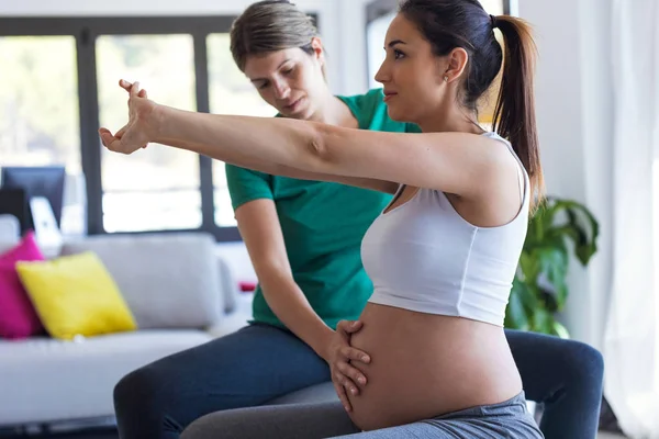 Fyzioterapeutka pomáhající krásné těhotné ženě při cvičení na Pilates s kuličková Příprava k porodu. — Stock fotografie