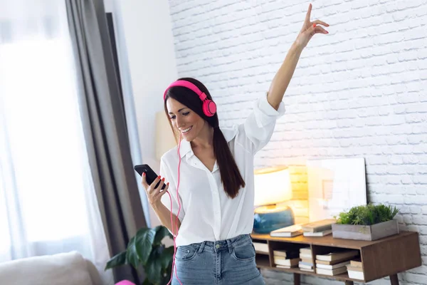 Hübsche junge Frau hört Musik mit Handy, während sie zu Hause im Wohnzimmer tanzt. — Stockfoto