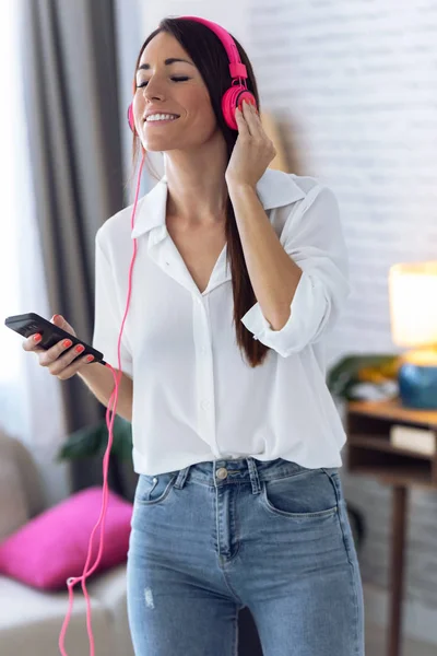 Mooie jonge vrouw luisteren naar muziek met mobiele telefoon tijdens het dansen in de woonkamer thuis. — Stockfoto
