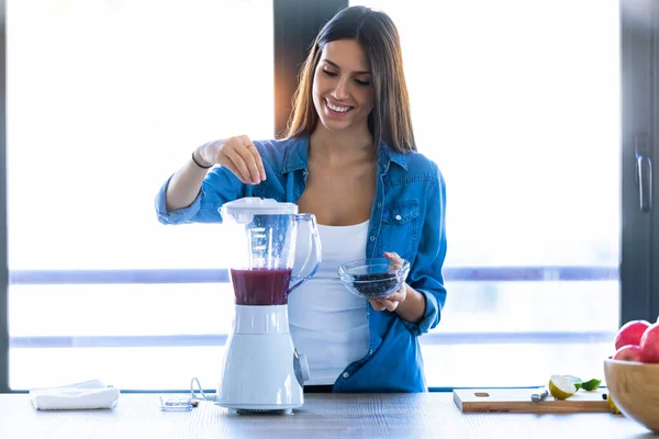 Mulher bonita preparando bebida de frutas no liquidificador para café da manhã fresco na cozinha em casa . — Fotografia de Stock