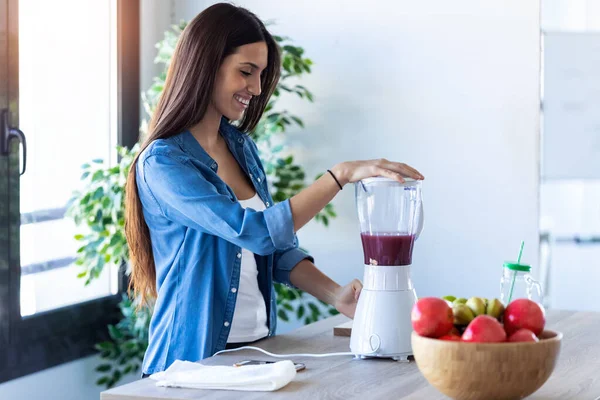 Mulher muito jovem misturando frutas no liquidificador para café da manhã fresco na cozinha em casa . — Fotografia de Stock