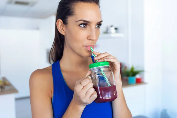 Vacker sportig ung kvinna dricker detox juice i köket hemma. — Stockfoto