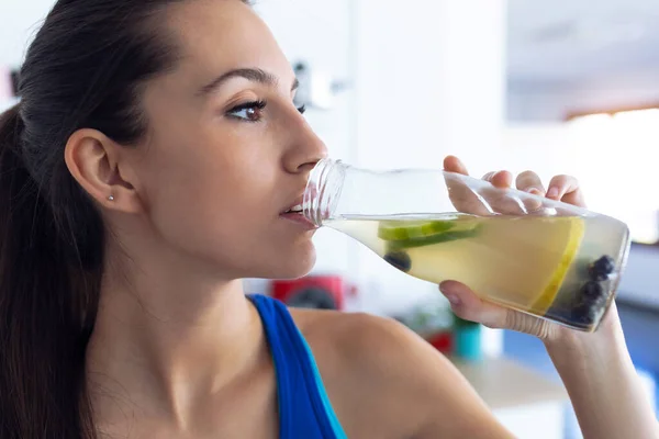 Bela jovem desportiva bebendo suco de desintoxicação na cozinha em casa . — Fotografia de Stock