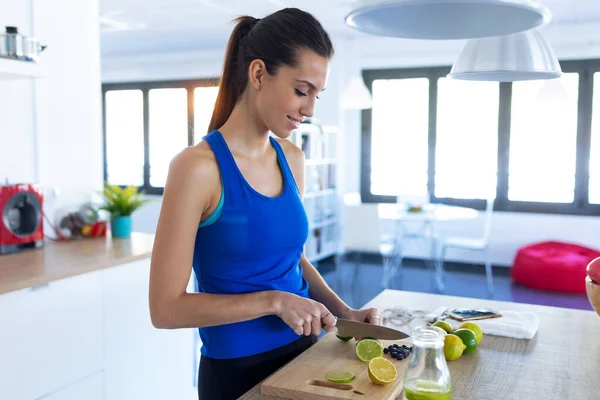 Sportieve jonge vrouw snijden limoenen tijdens het luisteren naar muziek in de keuken thuis. — Stockfoto