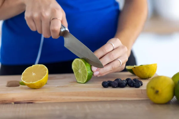 Woman's hands while she cutting limes over wooden table in the kitchen. — Stock Photo, Image