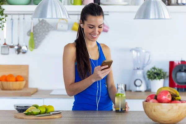 Evdeki mutfaktaki eğitimden sonra cep telefonuyla müzik dinleyen genç bir kadın.. — Stok fotoğraf