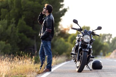 Motosikletli bir adam yolda yaşadığı bir arızadan sonra telefonda motorsikletinin sigortasıyla konuşuyor..