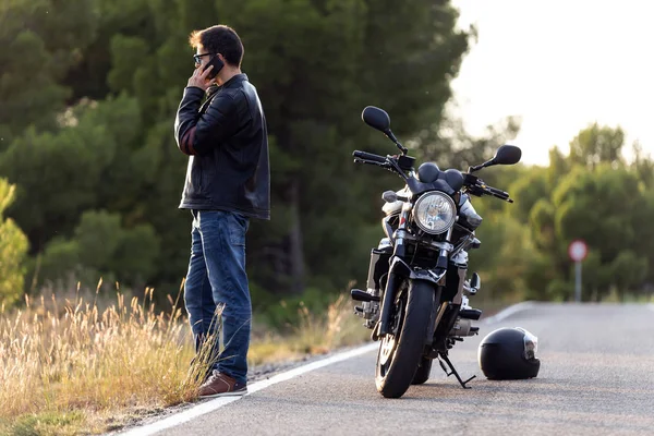 Motocyklista rozmawiający przez telefon z ubezpieczeniem motocykla po tym, jak doznał załamania na drodze. — Zdjęcie stockowe