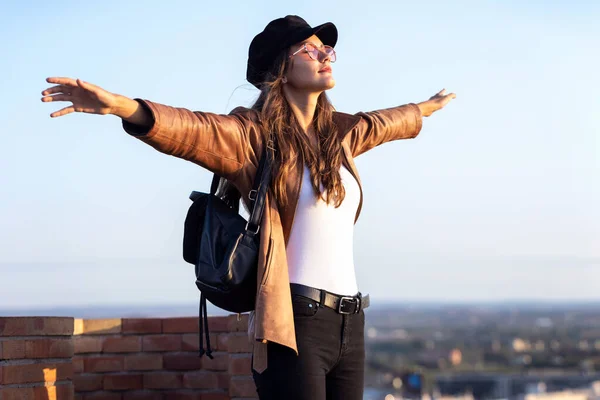 Mujer bastante joven disfrutando del tiempo y la puesta de sol mientras está de pie en la azotea . — Foto de Stock