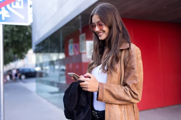 Hübsche junge Frau benutzt ihr Handy, während sie auf der Straße steht. — Stockfoto