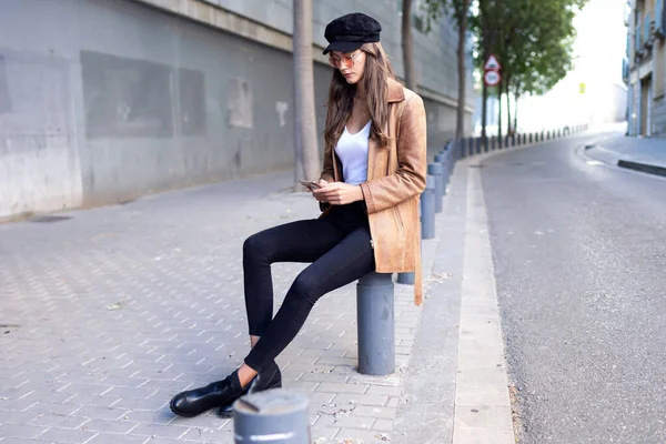 Mujer bastante joven usando su teléfono móvil mientras está sentada en la calle . — Foto de Stock