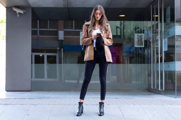 Mujer bastante joven usando su teléfono móvil mientras está de pie en la calle . — Foto de Stock