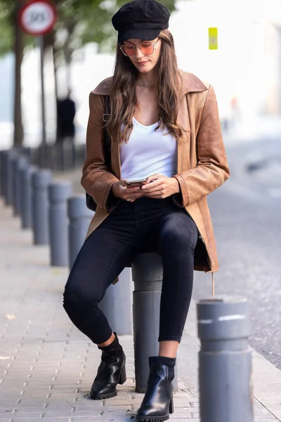 Mujer bastante joven usando su teléfono móvil mientras está sentada en la calle . — Foto de Stock