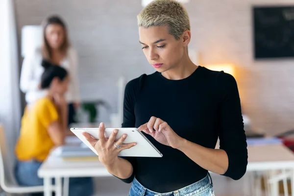 Концентрована молода жінка-підприємець використовує свій цифровий планшет, стоячи в офісі — стокове фото