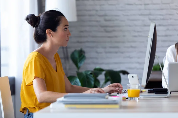 O tânără femeie de afaceri concentrată care lucrează cu computerul ei la birou . — Fotografie, imagine de stoc