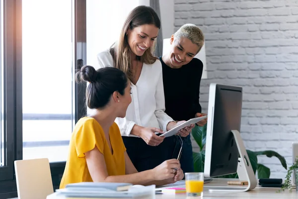 Tre moderna affärskvinnor pratar och granskar det senaste arbetet med datorn på en gemensam arbetsplats — Stockfoto