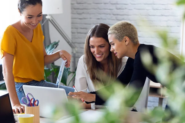 Três mulheres de negócios modernas conversando e revisando o mais recente trabalho feito no computador em um espaço de trabalho conjunto — Fotografia de Stock