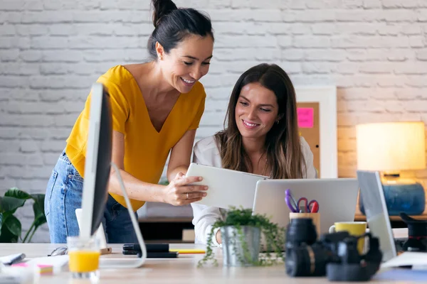 Två unga affärskvinnor pratar och granskar sitt senaste arbete i den digitala surfplattan på kontoret. — Stockfoto
