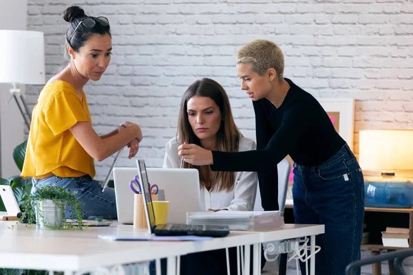 Tre moderna affärskvinnor pratar och granskar det senaste arbetet med datorn på en gemensam arbetsplats — Stockfoto