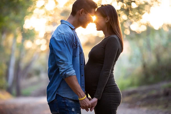 Unga snygga gravida par tittar på varandra medan poserar i parken. — Stockfoto