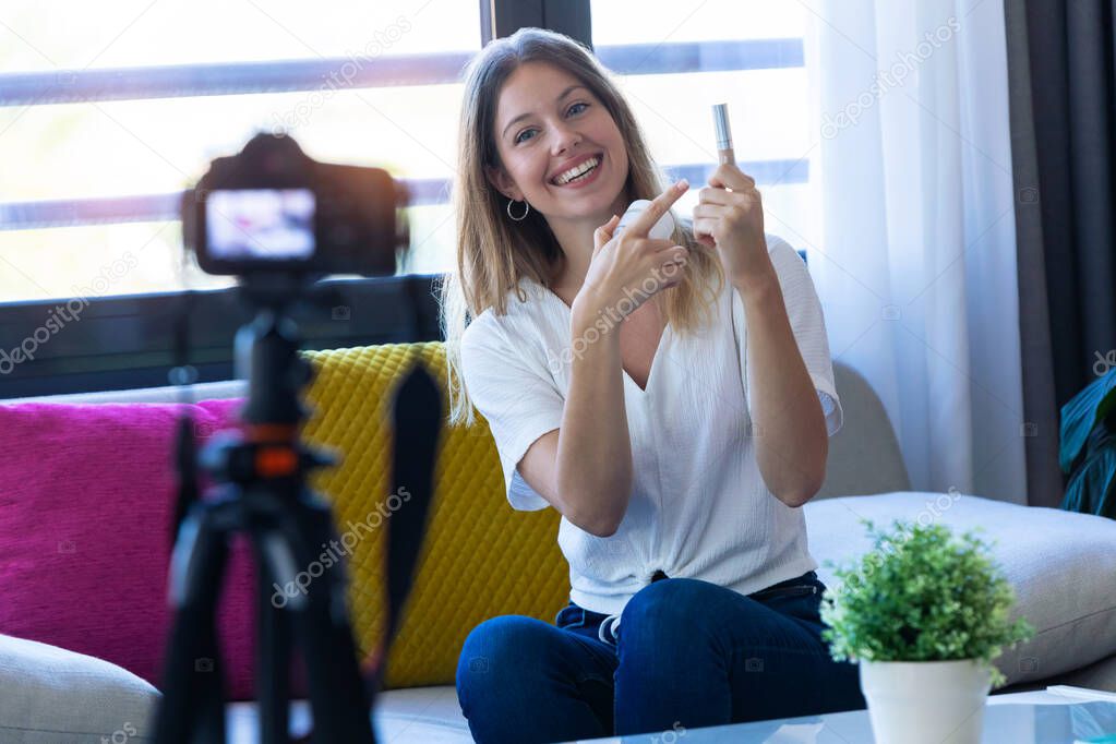 Pretty young woman blogger holding beauty products and smiling while making social media video