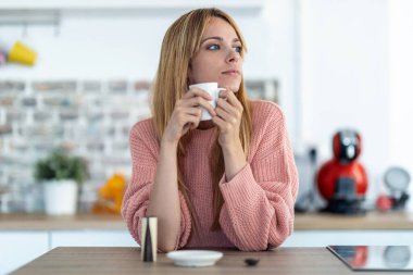 Sabahları mutfakta kahve içen düşünceli genç bir kadın..